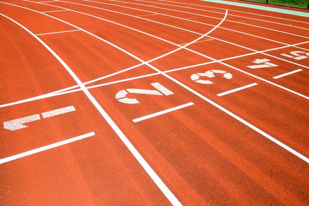 Nahaufnahme einer roten Laufbahn mit weißen Startnummern 1, 2, 3 und Markierungen für Laufstrecken.